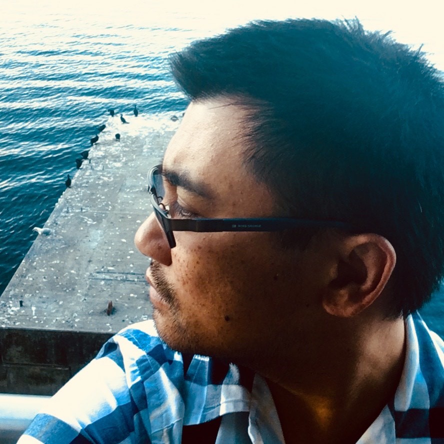 ID: Carlo wears eyeglasses and stares profile left to the ocean.