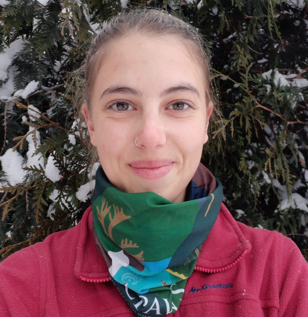 ID" Skye smiles near snowy tree with CPAWS-BC colourful neckwarmer and pick jacket.