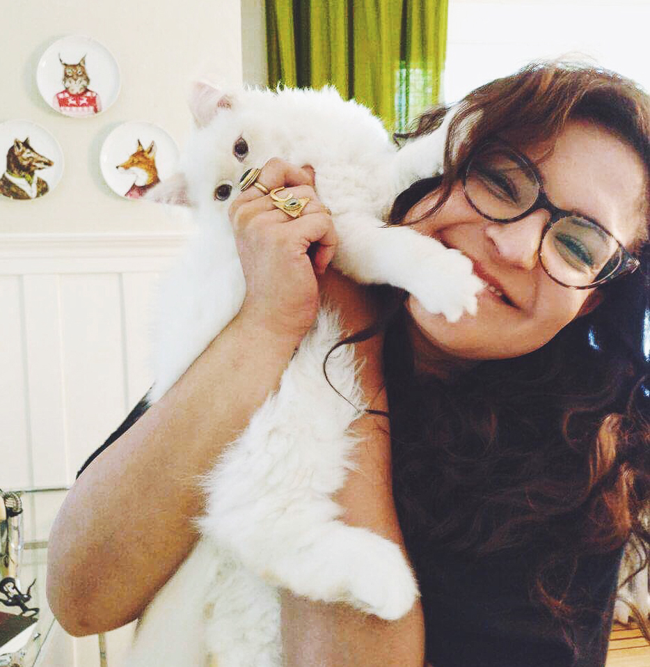 ID: Krstina wears eyeglasses, long hair smiles with white cat.