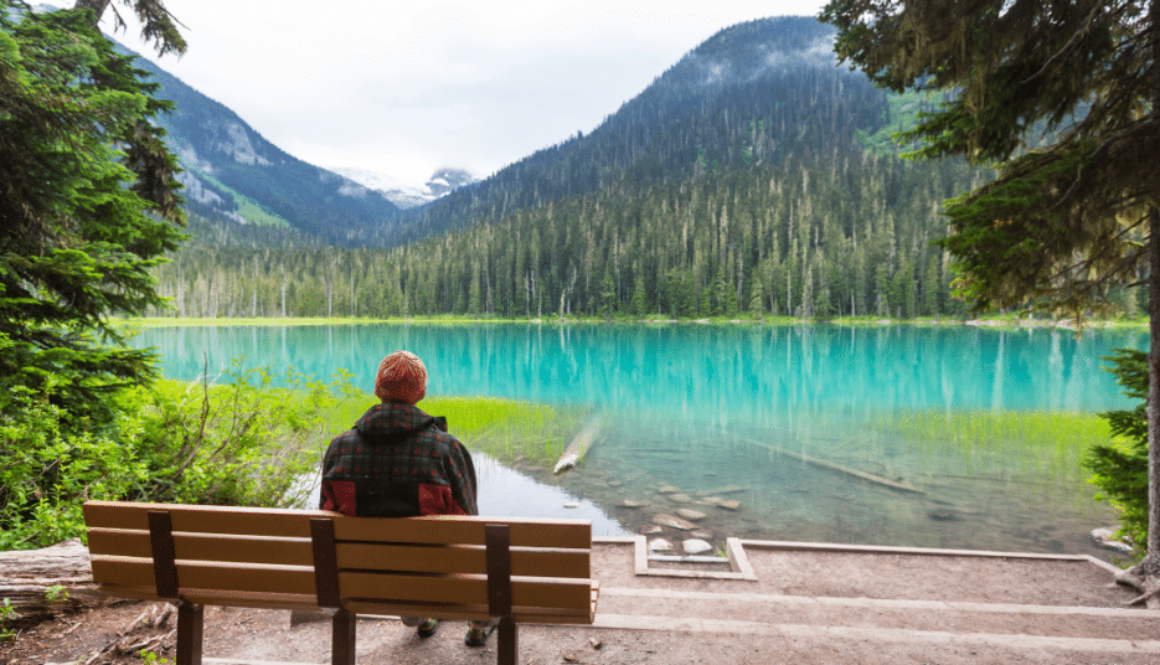 A person sits on a bench facing a turquoise glacial lake.