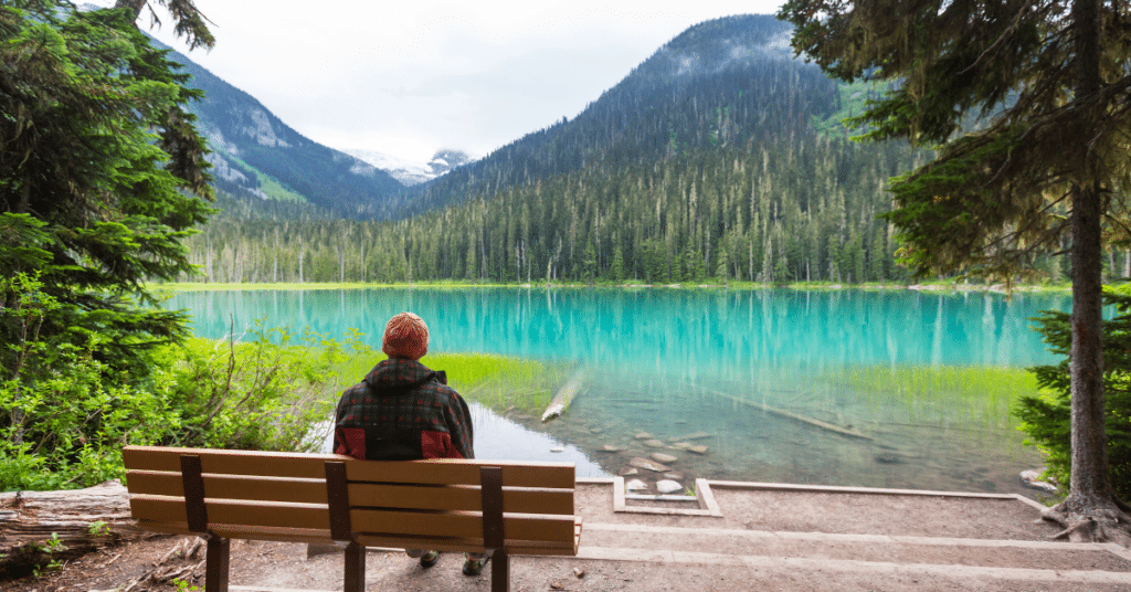 A person sits on a bench facing a turquoise glacial lake.