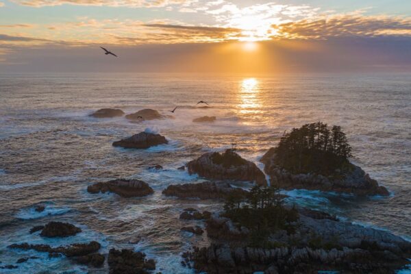 The sun sets behind the ocean with small forested islands in the foreground. Photo by: Markus Thompson