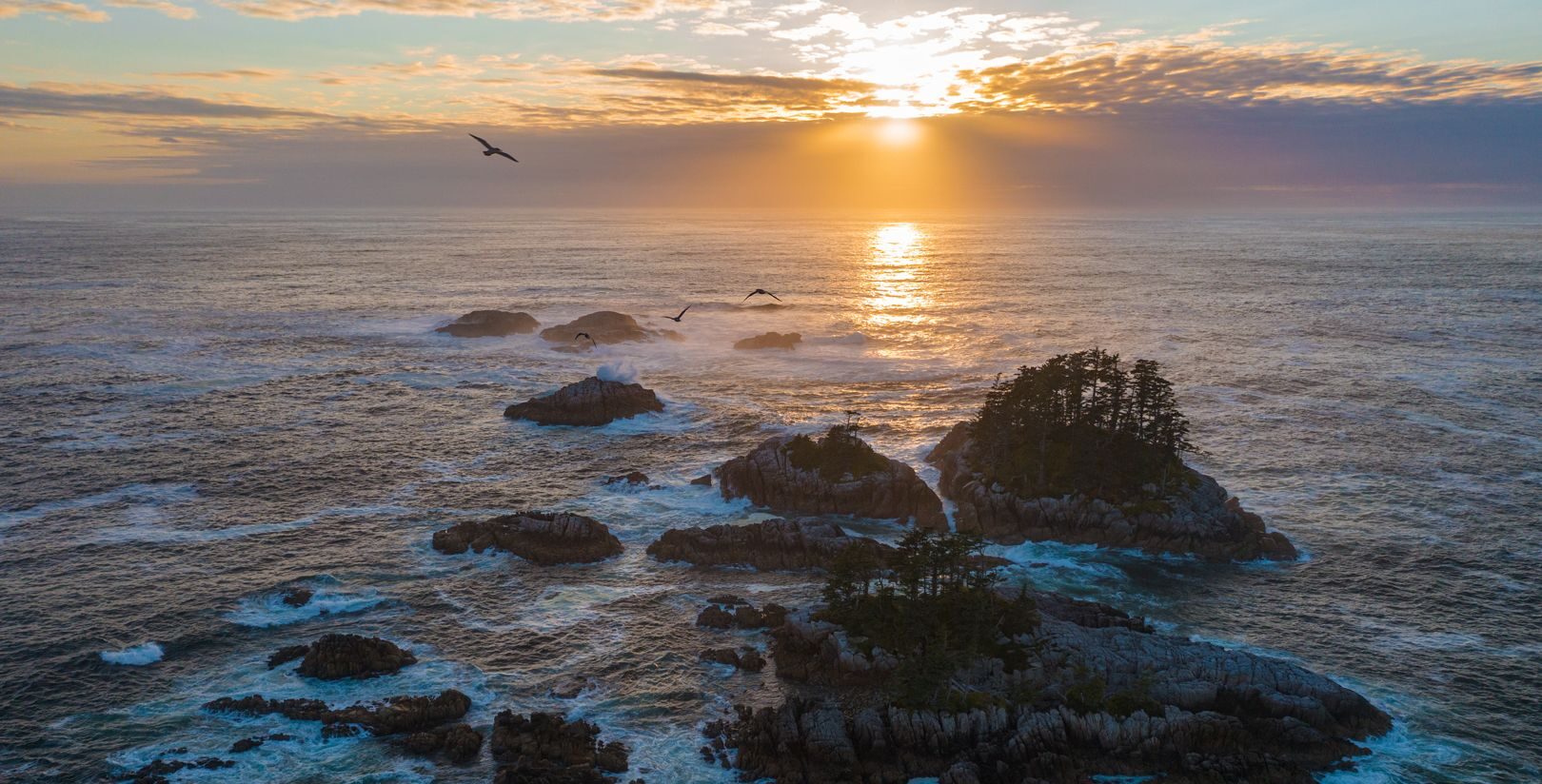 The sun sets behind the ocean with small forested islands in the foreground. Photo by: Markus Thompson